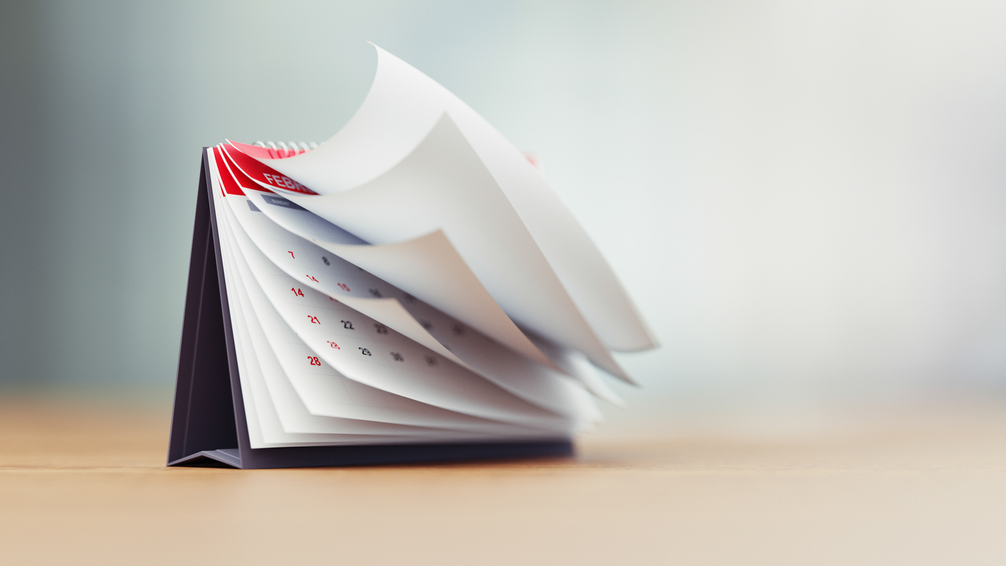 Pages of a red calendar standing over defocused background surface are folding.