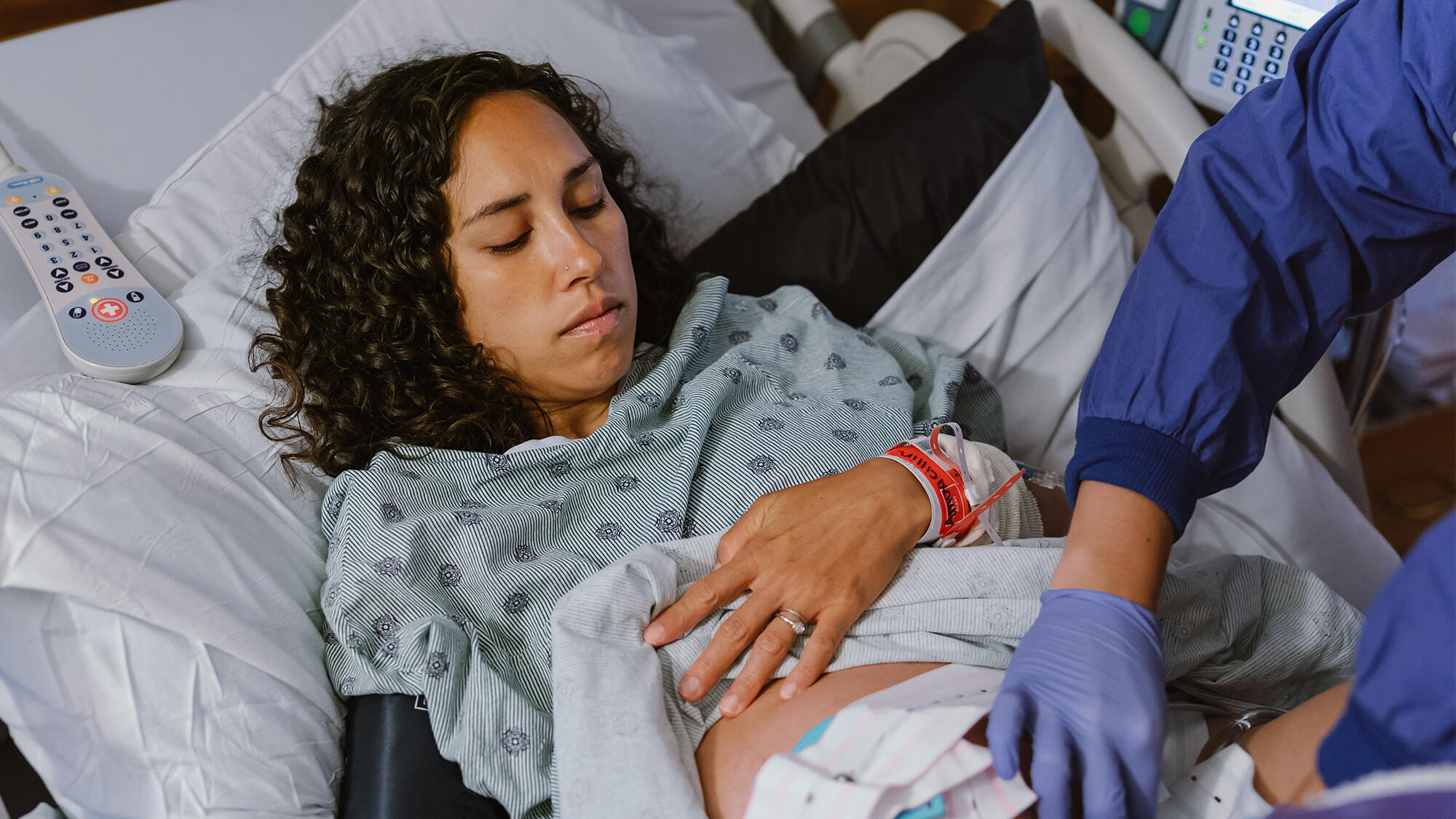 A pregnant woman lies in a hospital bed with medical staff checking her abdomen, preparing for or undergoing a medical procedure.