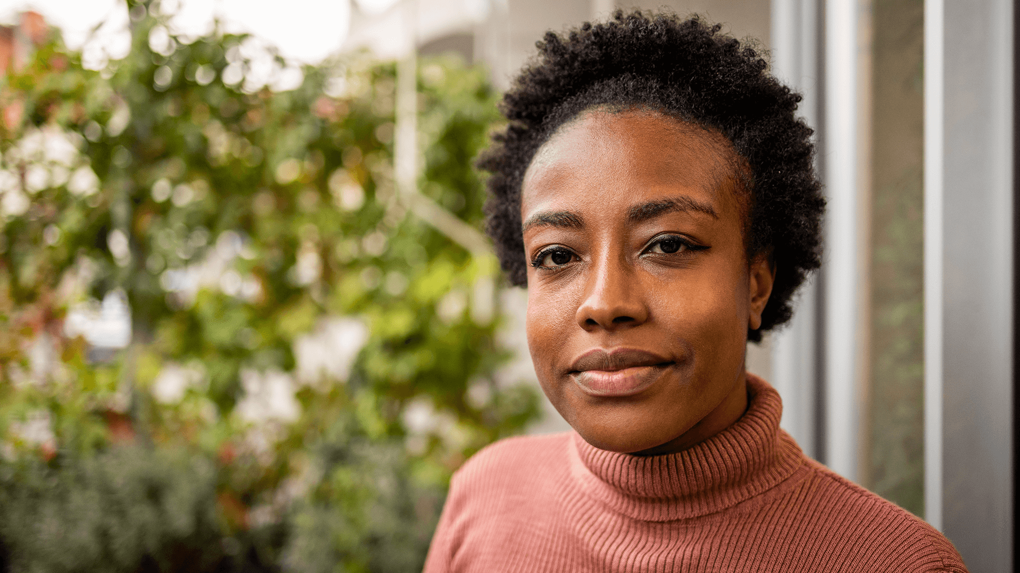 30 Something African American Woman with short black hair and a pink turtleneck